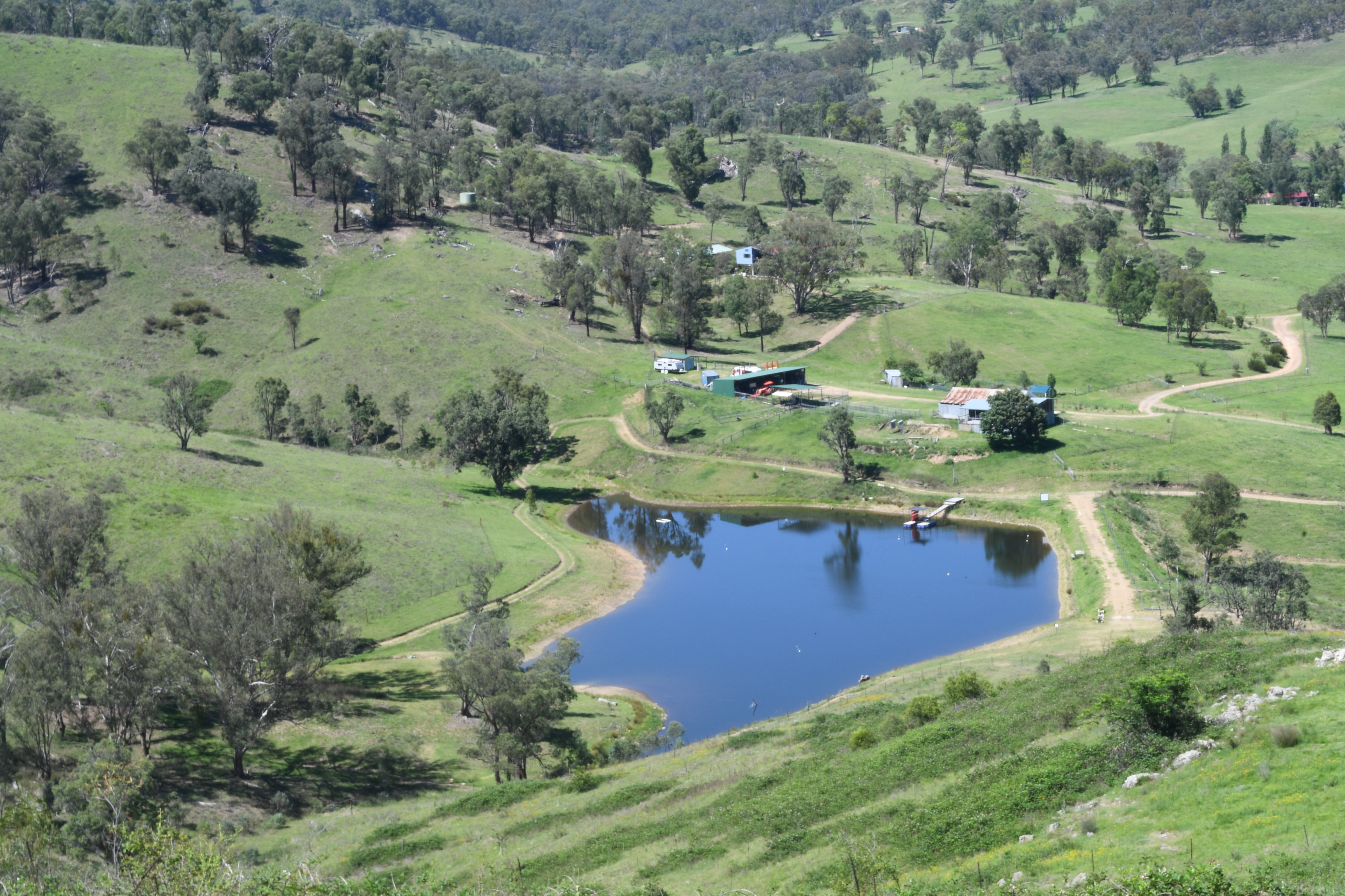 Looking down from the hill over the Springcart Farm dam, sheds and tracks in soft daylight